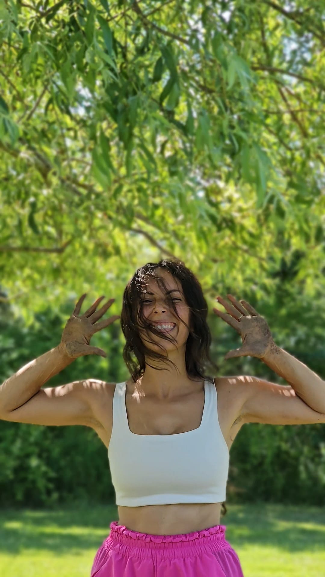 Sarah smiling outdoors under green leaves.